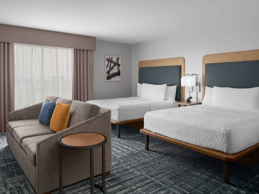 Ein Hotelzimmer mit zwei Betten, einem Sofa, einem kleinen Tisch und einem Fenster mit Vorhängen.