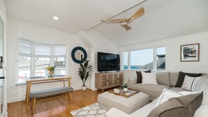 A modern living room with a large TV, a wooden bench, a sofa, and a view of the outside.