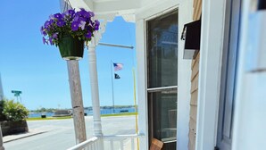 A wooden porch with a white railing, a table and two chairs, and a potted plant with colorful flowers.
