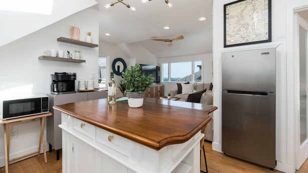 A modern kitchen with a wooden countertop, white cabinetry, a stainless steel refrigerator, and a ceiling fan.