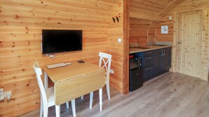 Ein Holzinnenraum mit an der Wand montiertem Fernseher, einem Esstisch mit Stühlen sowie einer Küchenzeile mit Schränken und Spüle.