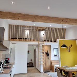 A modern kitchen with a built-in stove, a dining area with a wooden table, and a yellow accent wall. - Aussiedlerhof in Alleinlage. Großzügige Ferienwohnung (Rot am See)