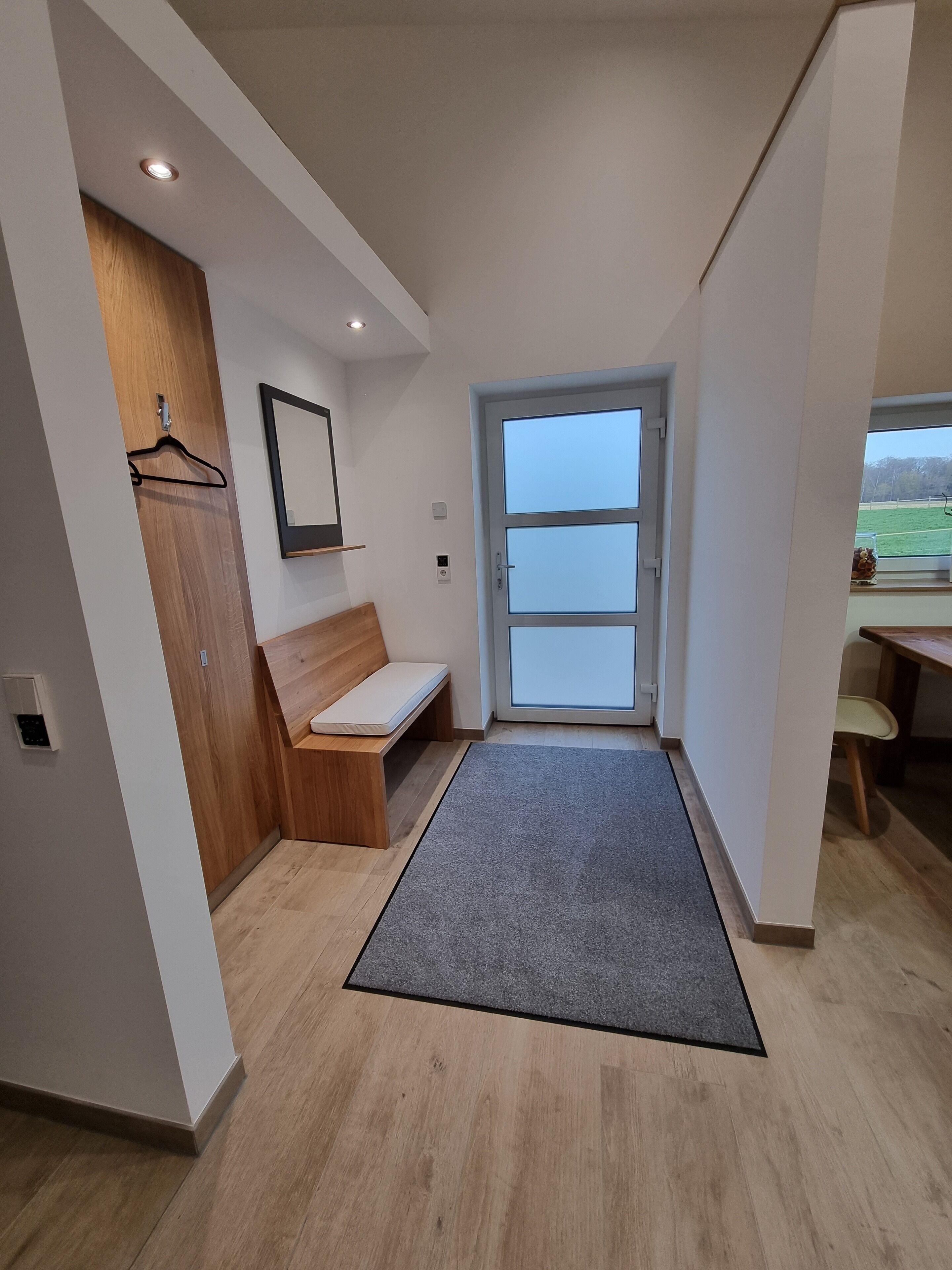 A modern hallway with a bench, a door with glass panels, and a view of the outdoors.
