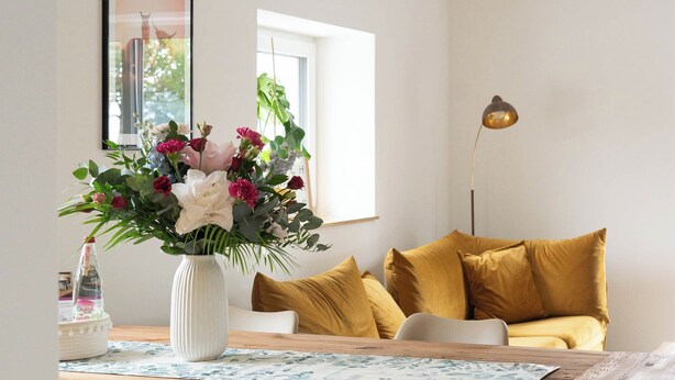 Un comedor con mesa de madera, sillas, un jarrón de flores y un sofá amarillo.