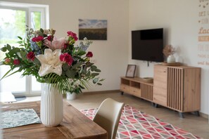 A dining area with a wooden table, a white vase with flowers, a TV, and a wooden cabinet. - Aussiedlerhof in Alleinlage. Großzügige Ferienwohnung (Rot am See)