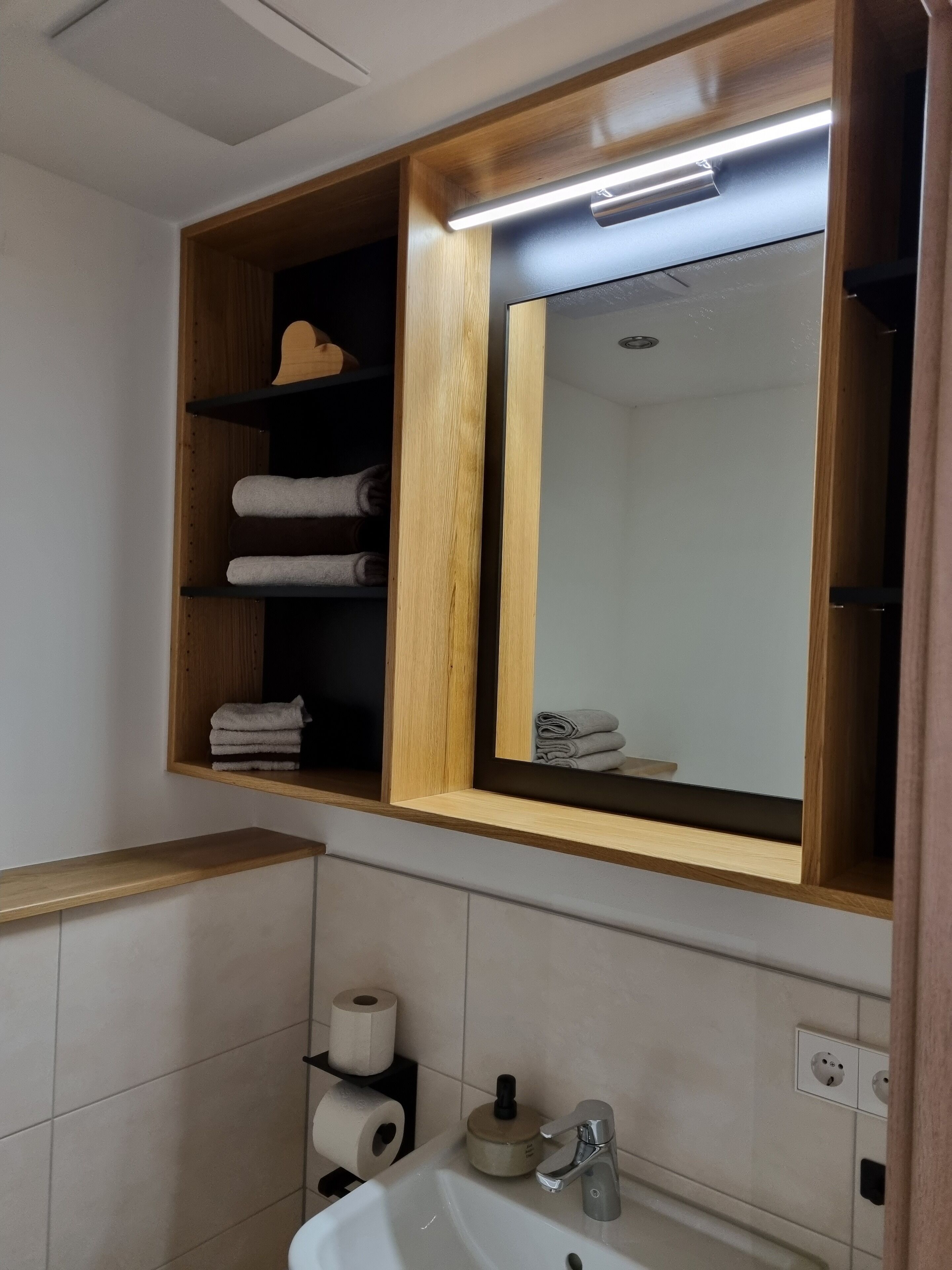A bathroom with a wooden vanity, a mirror, a sink, and shelves with towels.