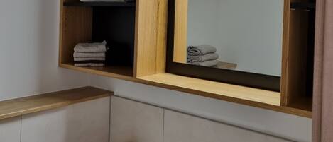 A bathroom with a wooden vanity, a mirror, a sink, and shelves with towels.