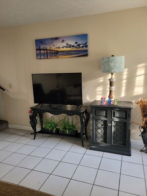 Ein Wohnzimmer mit Flachbildfernseher, einer dekorativen Lampe, einem Gemälde und einer Vitrine mit Pflanze.