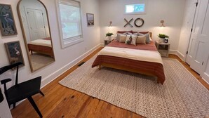 A bedroom with a bed, a ceiling fan, a mirror, a window, and a wall-mounted light fixture. - Millhouse in Downtown Jefferson (Jefferson)