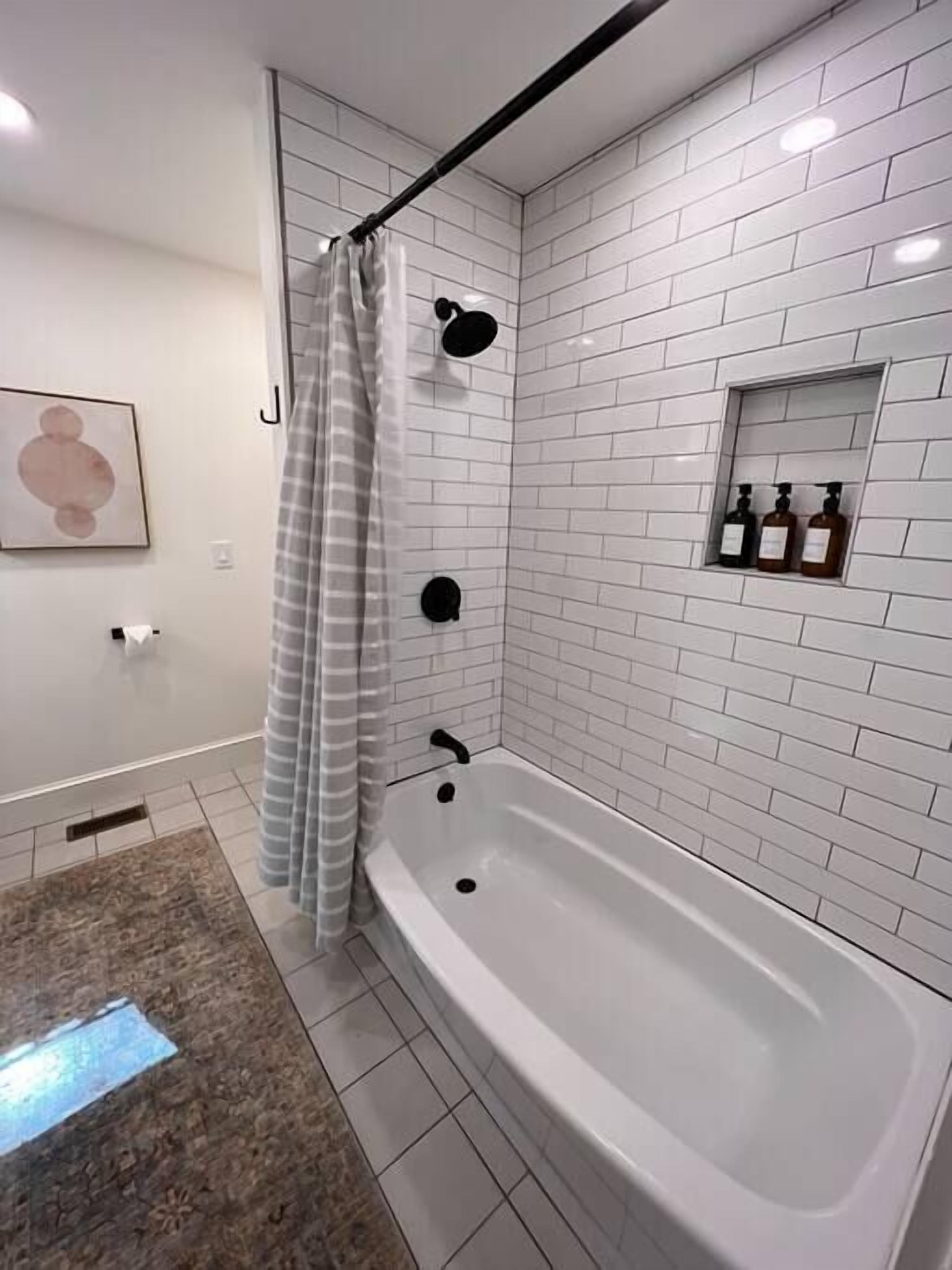 A modern bathroom with a freestanding bathtub, white subway tiles, a shower curtain, and a small shelf with toiletries.