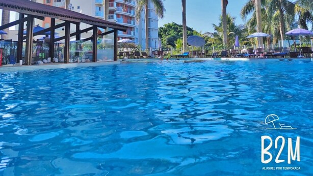 A swimming pool with palm trees and a multi-story hotel building in the background. - Beto Carrero, Vista Espetacular do Mar, Home Club (Penha)