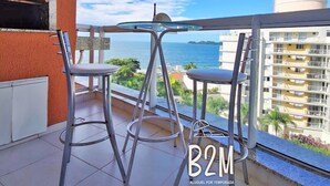 A balcony with two metal chairs, a glass table, and a view of the sea and buildings. - Beto Carrero, Vista Espetacular do Mar, Home Club (Penha)