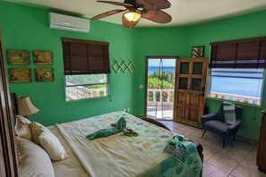 A bedroom with a bed, a chair, a ceiling fan, and a view of the outdoors.