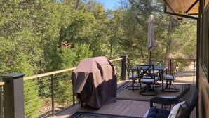 Una terraza techada al aire libre con una parrilla, mobiliario de mimbre y vistas del bosque circundante.