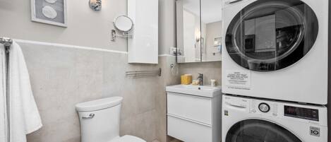 Un baño moderno con inodoro, lavabo y lavadoras apiladas.