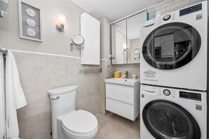 Une salle de bain moderne équipée de toilettes, d’un lavabo et de machines à laver superposées.