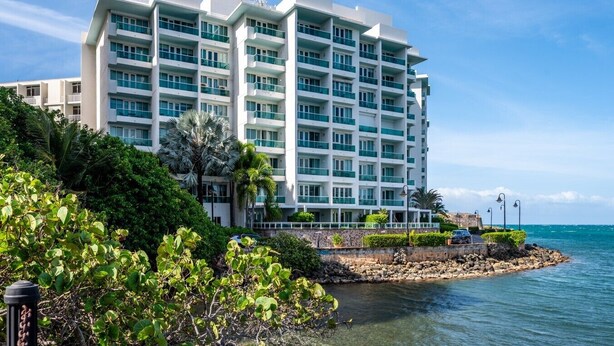 Un hôtel à plusieurs étages, doté de balcons, situé en bord de mer, sur une côte rocheuse.