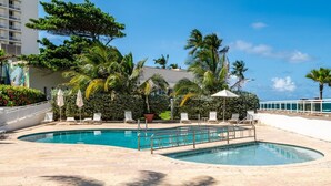 Un espace piscine comprenant deux piscines, des chaises longues, des parasols et des palmiers.
