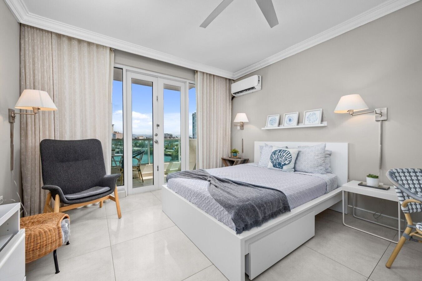 A bedroom with a bed, a chair, a small table, a lamp, and a view of the outdoors.