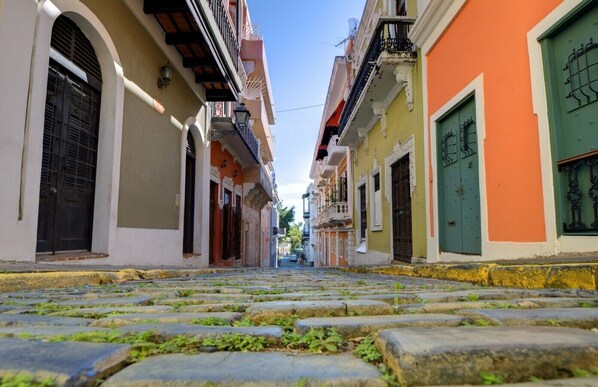 A narrow cobblestone street flanked by colorful buildings with balconies and arched doorways.