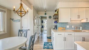 A kitchen with white cabinets, a chandelier, and a blue patterned rug. - Ocean-View Balcony: Carolina Beach Condo! (Carolina Beach)