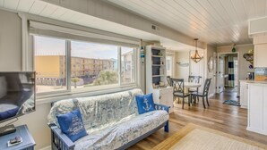A living room with a sofa, TV, and large windows overlooking a building. - Ocean-View Balcony: Carolina Beach Condo! (Carolina Beach)
