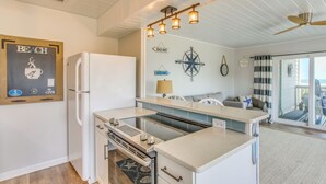 A kitchen with a white refrigerator, a stove, and a countertop. There are wall decorations including a compass and signs. - Ocean-View Balcony: Carolina Beach Condo! (Carolina Beach)