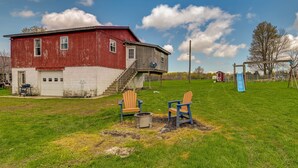 A red barn with a white lower section, a blue slide, and two Adirondack chairs on a grassy field. - Upstate New York Vacation Rental Near Cooperstown! (Jordanville)