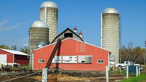 A red barn with a metal roof, surrounded by large silos and a white truck parked nearby. - Upstate New York Vacation Rental Near Cooperstown! (Jordanville)
