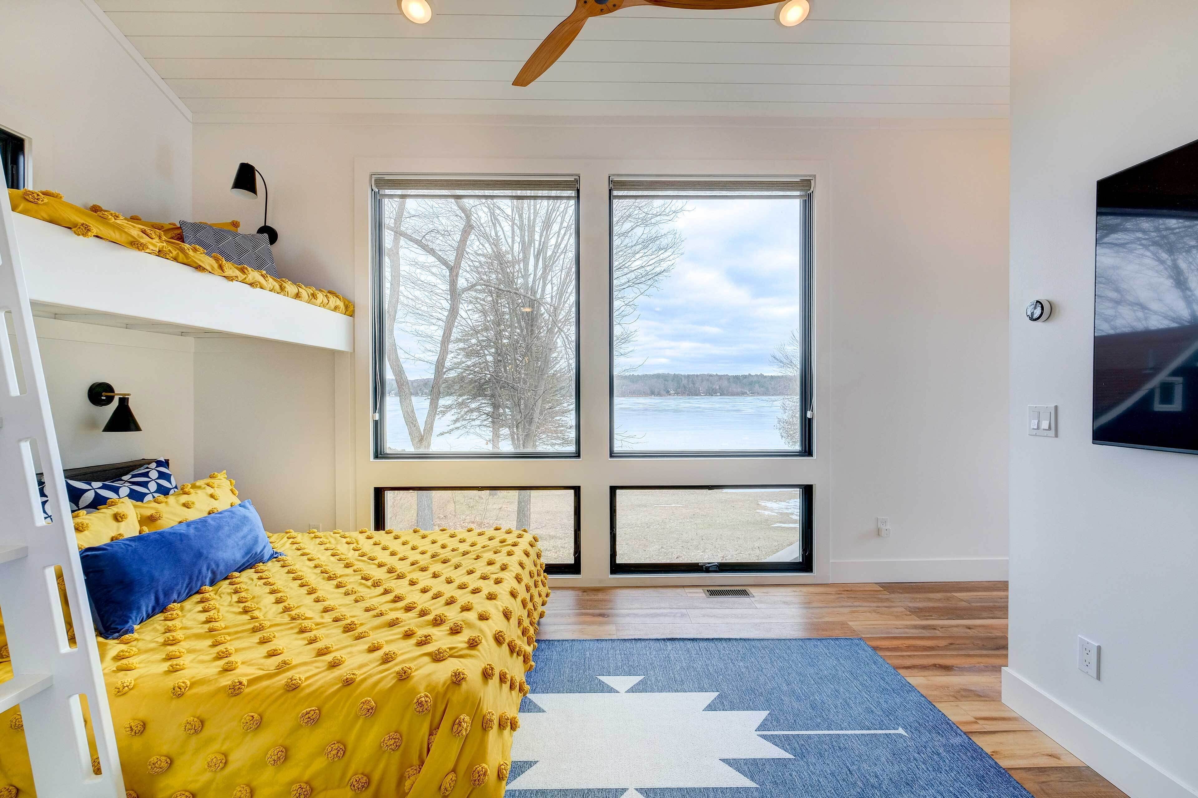 Una habitación con una cama litera, un ventanal con vistas a árboles y una masa de agua, y un televisor de pared.