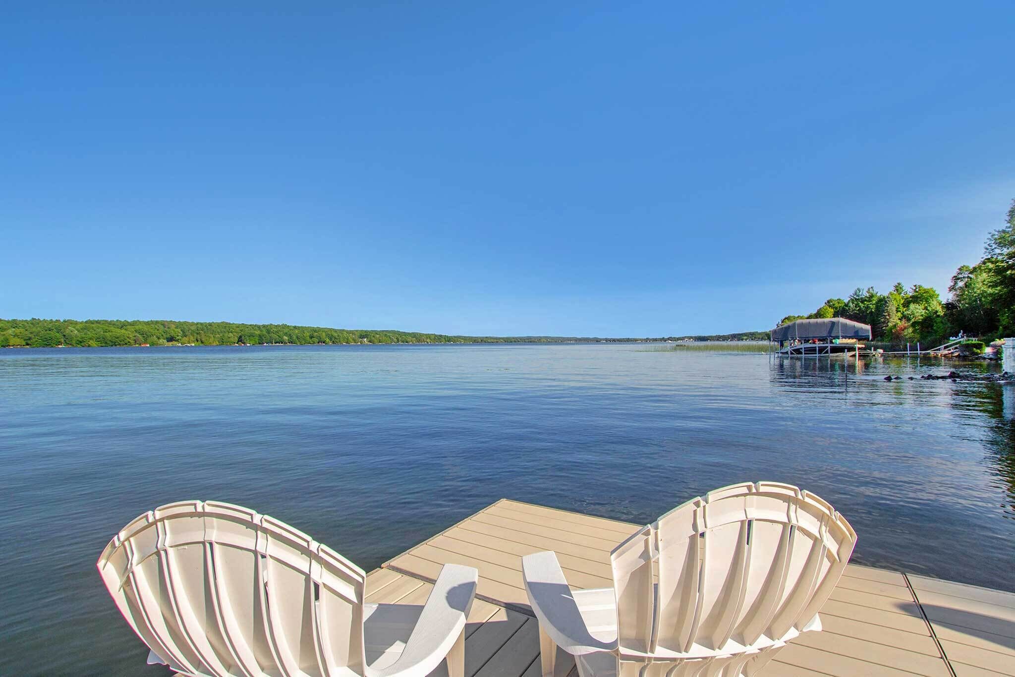 Une jetée en bois avec deux chaises Adirondack blanches, toutes deux tournées vers un lac paisible.