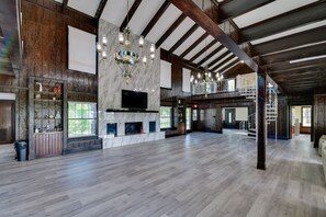A spacious room with a fireplace, wooden beams, and a chandelier. - Private Pool: Pilot Point Home on 45 Acres (Pilot Point)