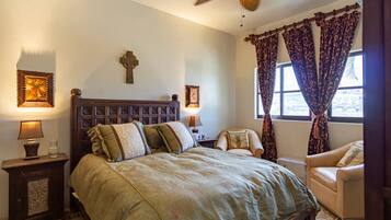 A bedroom with a large bed, two bedside tables with lamps, a cross on the wall, and a window with curtains.