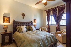 Une chambre à coucher avec un grand lit, deux tables de chevet avec des lampes, une croix accrochée au mur et une fenêtre avec des rideaux.