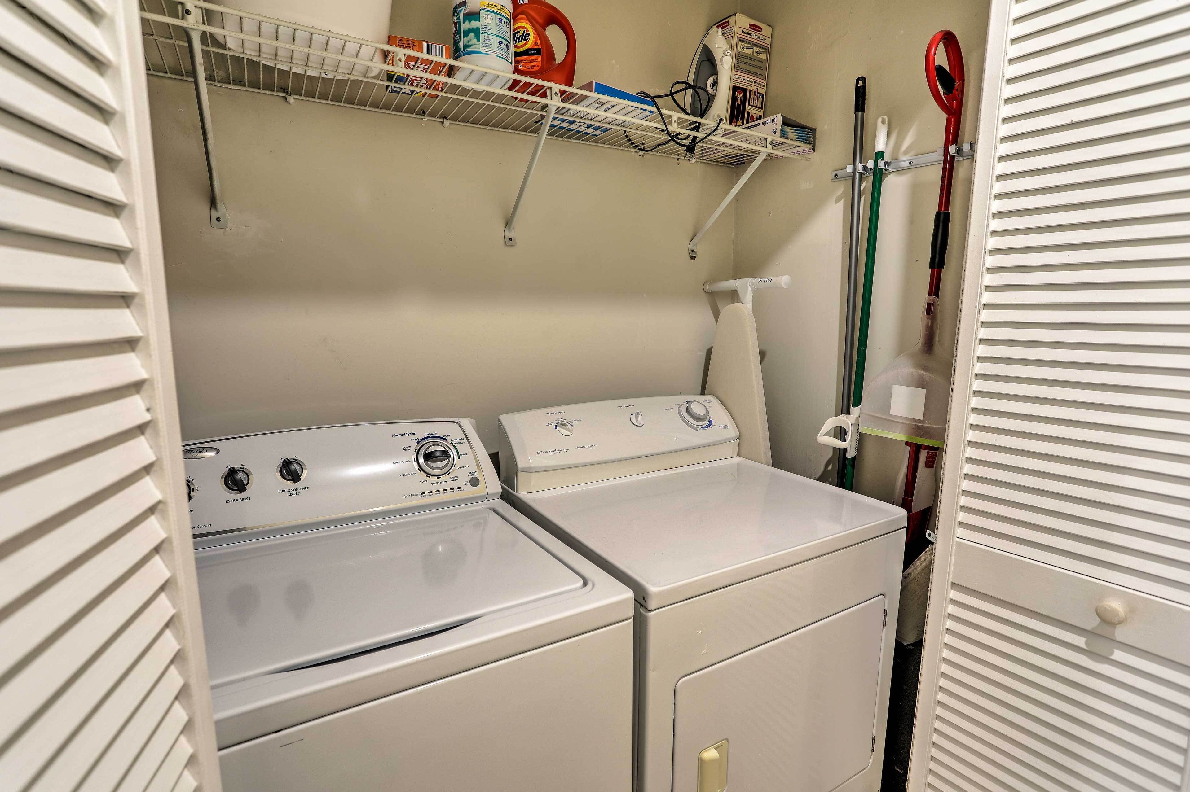 A laundry area with two white washing machines, a shelf with cleaning supplies, and a mop on the wall.