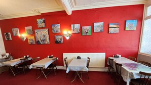 A restaurant with red walls, multiple tables with checkered tablecloths, and various paintings on the wall. - Moorfield Hotel (Blackpool)