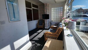 A sunlit room with a sofa, a chair, a table, and a TV. - Moorfield Hotel (Blackpool)