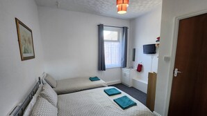 A room with two beds, a window with curtains, a TV mounted on the wall, and a wooden door. - Moorfield Hotel (Blackpool)