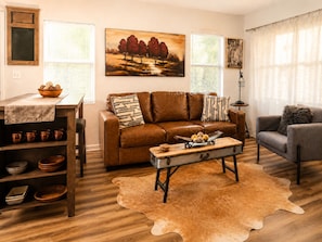 A living room with a brown leather sofa, a wooden coffee table, a grey armchair, and a cowhide rug.
