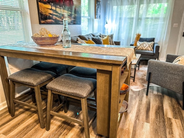 A wooden dining table with three stools, a bottle, and a woven basket on it.
