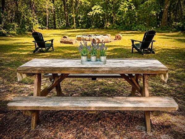A wooden picnic table with two chairs, surrounded by a grassy area with trees in the background. - Willis Oaks Country Cottage (Levy County)