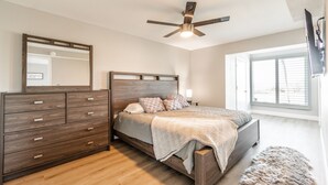 Ein Schlafzimmer mit einem hölzernen Bett, einer Kommode, einem Deckenventilator und einem großen Fenster.