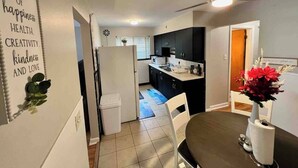 Eine moderne Küche mit dunklen Schränken, einem weißen Kühlschrank und einem Essbereich mit Tisch und Stühlen.