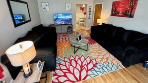 Ein Wohnzimmer mit einer Couch, einem Couchtisch, einem Fernseher und einem Teppich mit Blätermotiv.