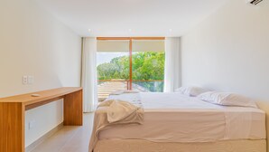 A modern bedroom with a large bed, a wooden bedside table, and a view of greenery through a sliding glass door.