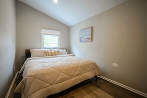 A bedroom with a bed, a window, and a painting on the wall.