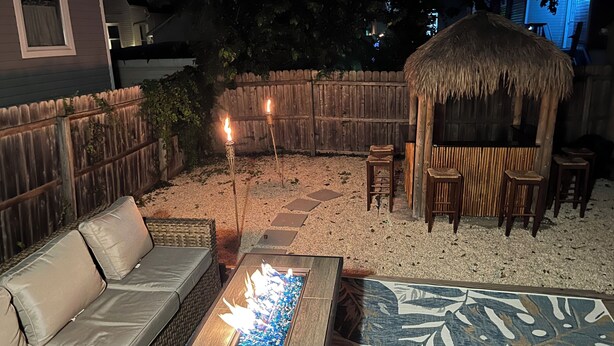Ein Patio mit bequemen Sitzmöglichkeiten, einer Feuerstelle und einer reetgedeckten Struktur.