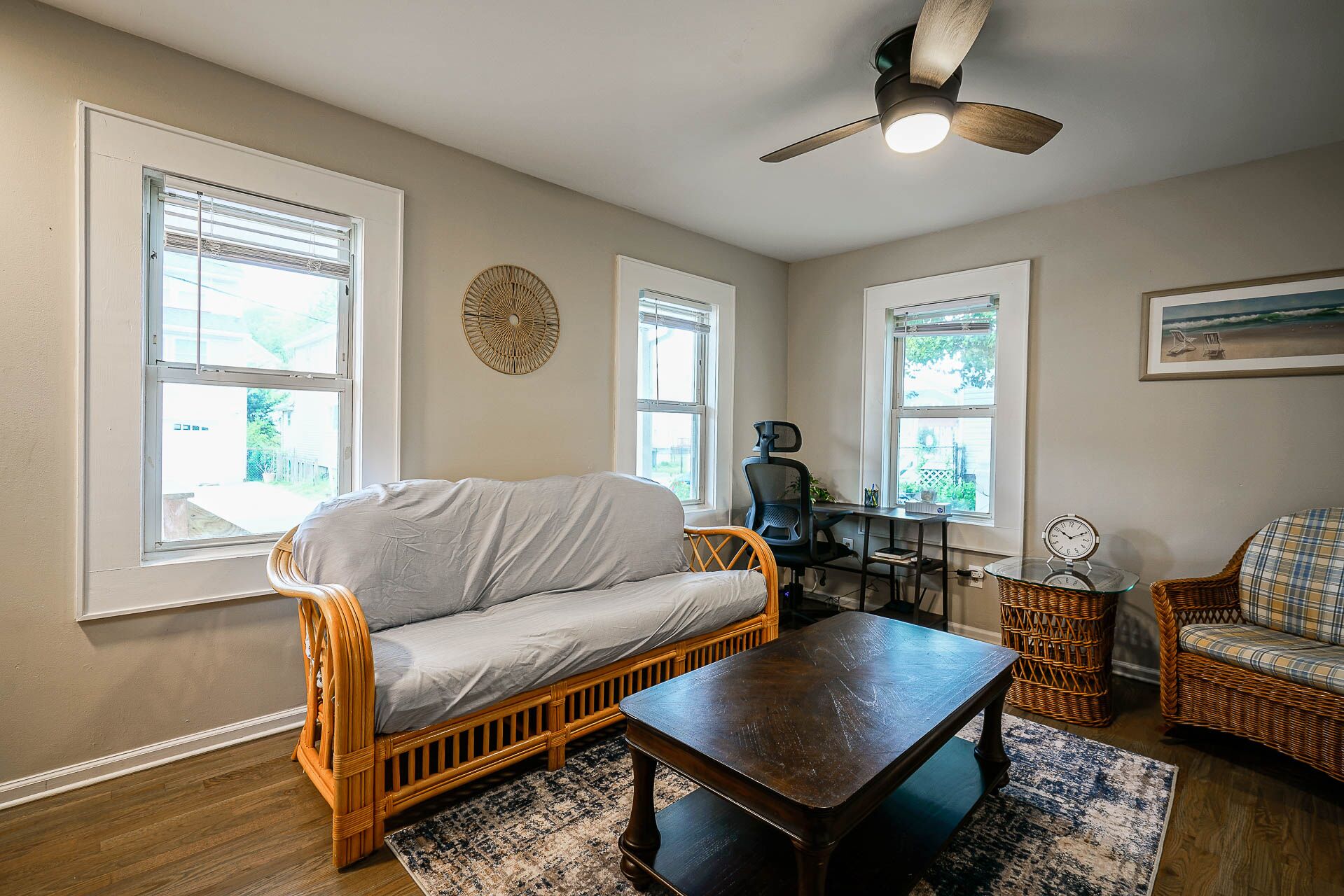 A living room with a sofa, a coffee table, wicker chairs, and a ceiling fan.