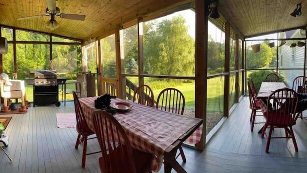 Ein überdachter Essbereich im Freien mit Tisch für zwei Personen, einem Grill und Blick auf die umliegende Grünfläche.