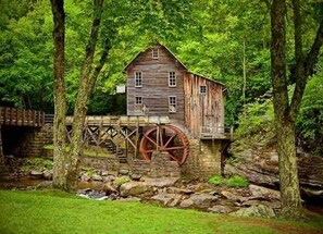 Eine rustikale Holz-Mühle mit einem großen Wasserrad, umgeben von üppigem Grün und einer Steinbrücke.